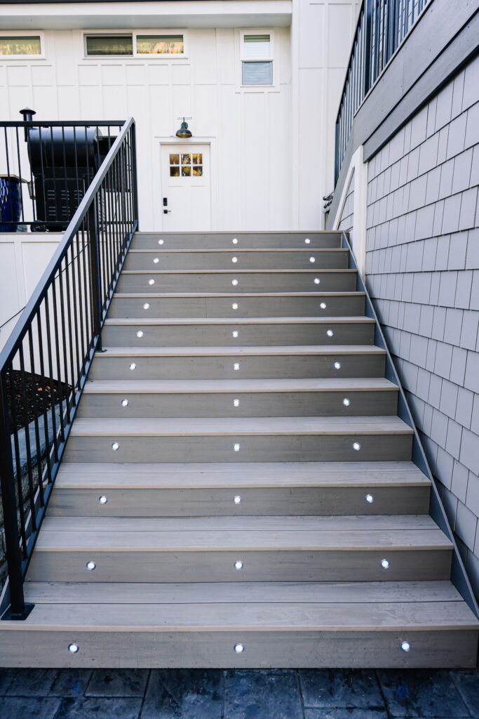 horizontal steel rod railing on stairs with stair lights on grey composite decking with siding on house